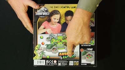 back of ravenous raptors game box showing pre-teen kids playing the game and neil dandy's finger pointing to the qr code