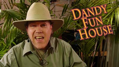 neil dandy wearing jungle explorer outfit in front of foliage next to dandy fun house logo