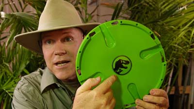 neil dandy holding the game field from ravenous raptors game and pointing out the jurassic world logo in the center
