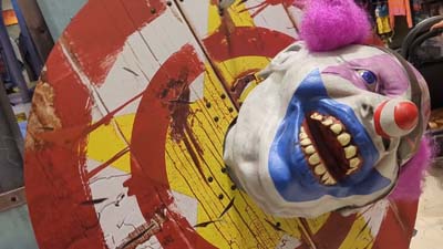 decapitated clown head on a rotating target board with knives sticking out of it