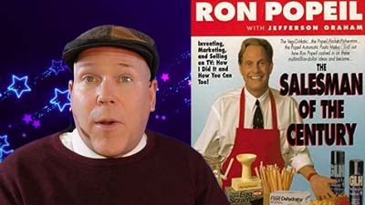neil dandy with a picture of the cover of ron popeil's autobiography, salesman of the century