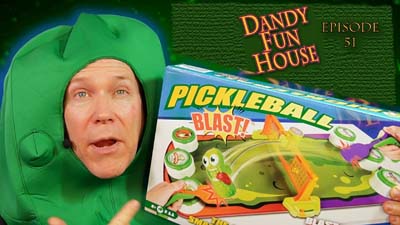neil dandy in a pickle costume holding the game of pickleball blast
